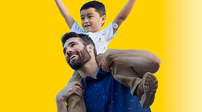 Man with boy on his shoulders. The boy has a Libre 2 sensor on his arm