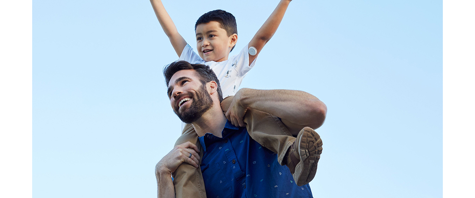 Father holding his son on his shoulders with a blue sky behind them