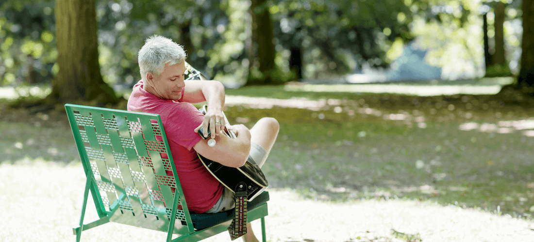 Người đàn ông ngồi chơi đàn trong công viên trong lúc quét cảm biến FreeStyle Libre với đầu đọc