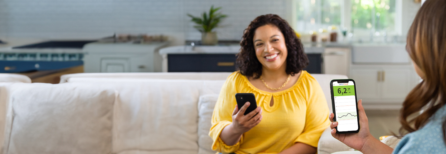 Kvinde i gul bluse smiler og holder en smartphone