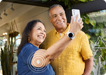 A woman wearing a FreeStyle Libre sensor is showing her glucose data on her smartphone to here significant other.