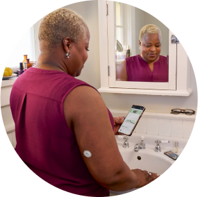 Woman standing by the mirror wearing a FreeStyle Libre sensor and checking her blood glucose on a smartphone