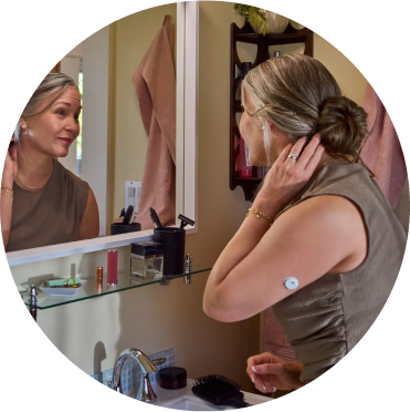 Woman by the bathroom mirror wearing a FreeStyle Libre 3 Plus sensor
