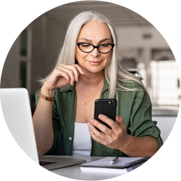 Woman looking at her smartphone as she sits at a desk in front of a computer