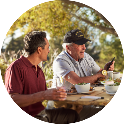 Two men eating a meal at a picnic table, with the older man wearing a FreeStyle Libre sensor