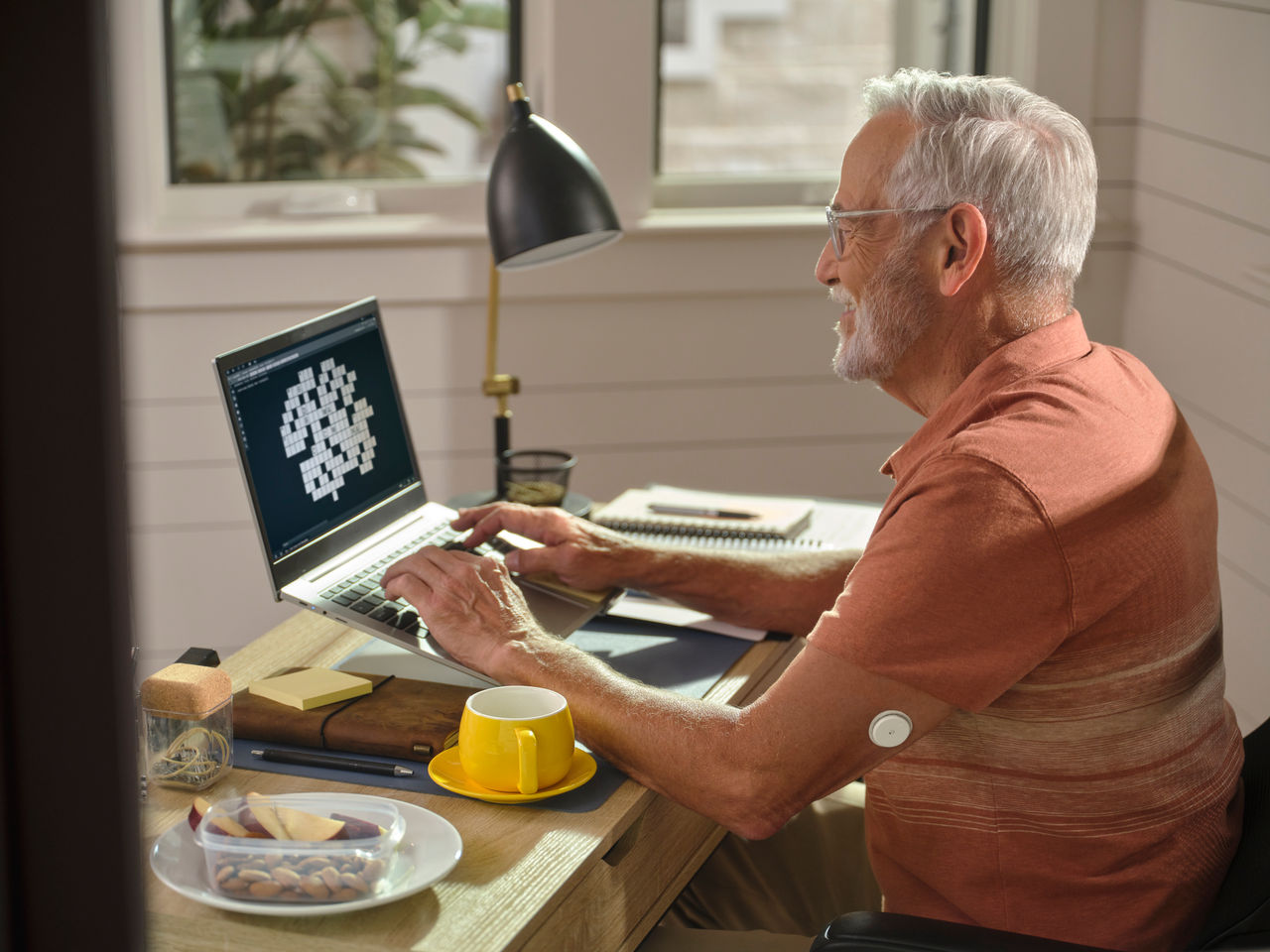 Μεσήλικας άντρας με αισθητήρα δουλεύει στον υπολγιστή του και δίπλα του έχει σνακ