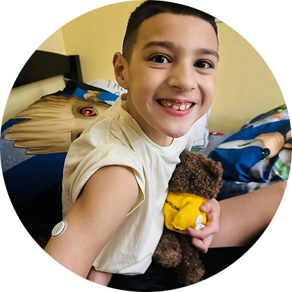 A little boy wearing a sensor, hugging his teddy bear and smiling