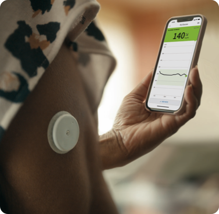 A close-up of FreeStyle Libre sensor attached on a patient's upper arm while they are holding a phone and checking their glucose readings