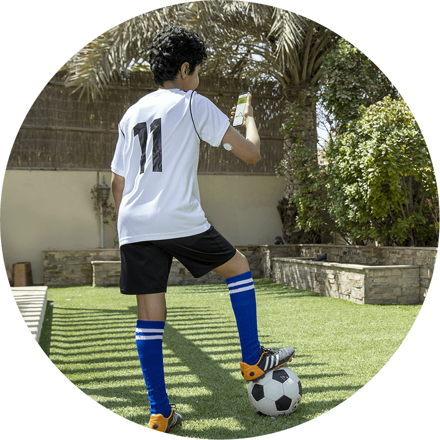 A child in football gear, wearing a Libre 2 sensor and checking his glucose readings on his phone