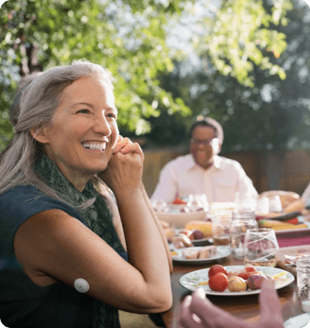 A woman eating outside and smiling while wearing a sensor
