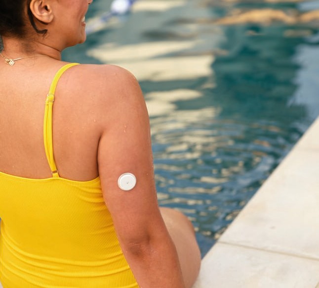 Femme assise au bord d'une piscine avec un capteur sur le haut du bras.