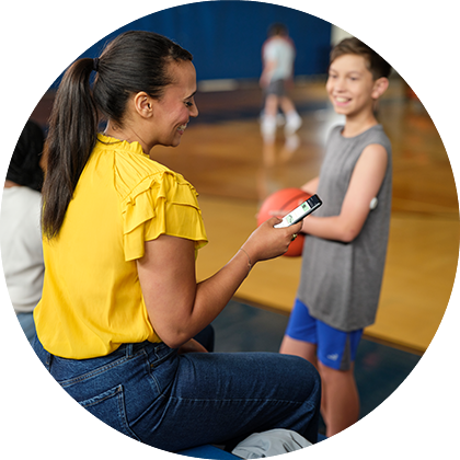 Une mère consultant l'application LibreLinkUp pendant que son fils, qui porte un capteur FreeStyle Libre, tient un ballon de basket dans une salle de sport