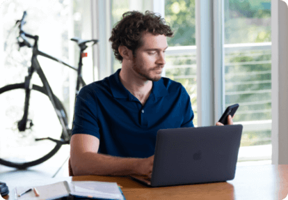Man looking at his mobile device while looking at a laptop
