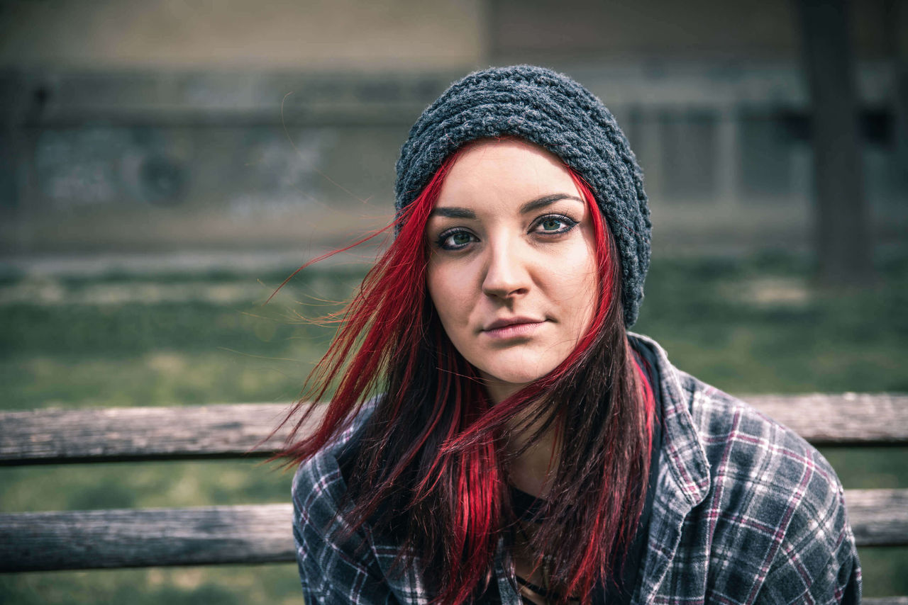 Young beautiful red hair girl sitting alone outdoors on the wooden bench with hat and shirt feeling anxious and depressed after she became a homeless person close up portrait , Young beautiful red hair girl sitting alone outdoors on the wood