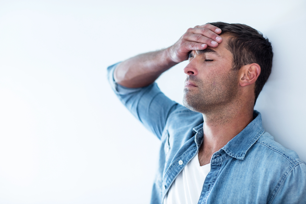 Close-up of upset man leaning on wall with hand on forehead