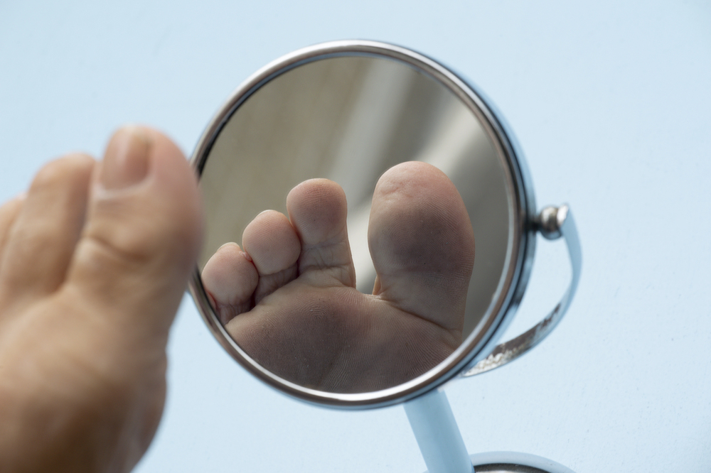 Person looking at the sole of the foot in a mirror, to check if there is no diabetic foot, as possible sores