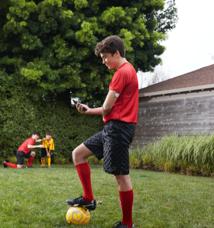 Rapaz com uma bola nos pés a olhar para o telemóvel