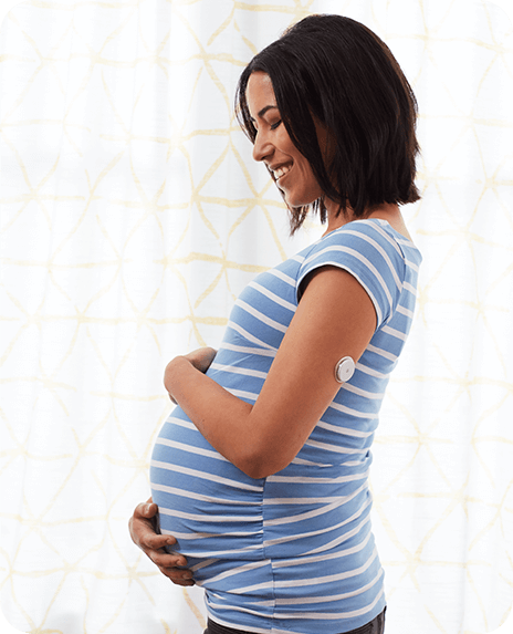 A pregnant woman standing and smiling while hugging her belly