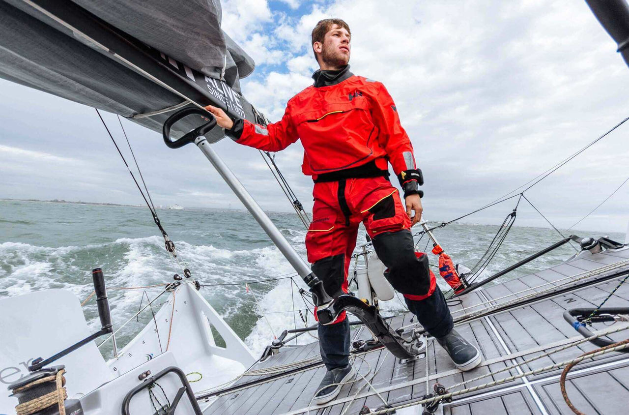 Man standing on a boat in the ocean wearing a waterproof suit.