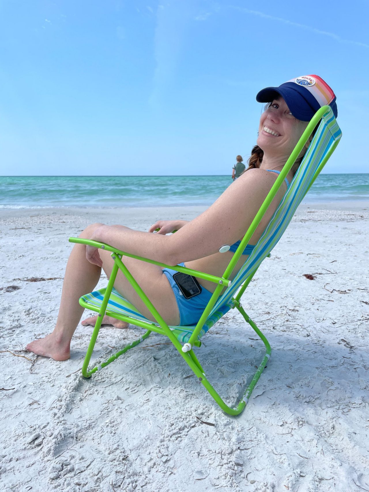 Erin, blog author, sitting on a beach chair smiling in frot of the ocean with FreeStyle Libre Sensor visible on the back of her upper arm