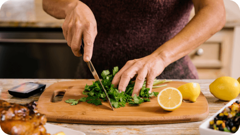 Hands chopping parsley on a cutting board next to lemons.