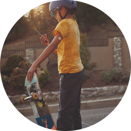 child with sensor, wearing a helmet and holding a skateboard, checking his phone