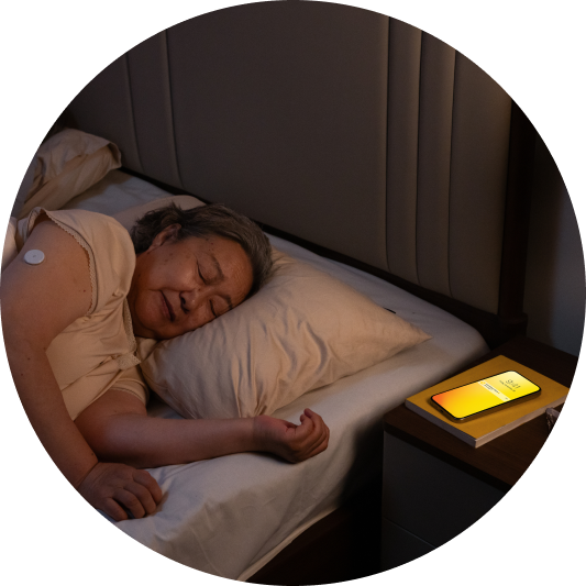 an image of a woman sleeping with a glucose alarm on her phone and a visible sensor on her arm