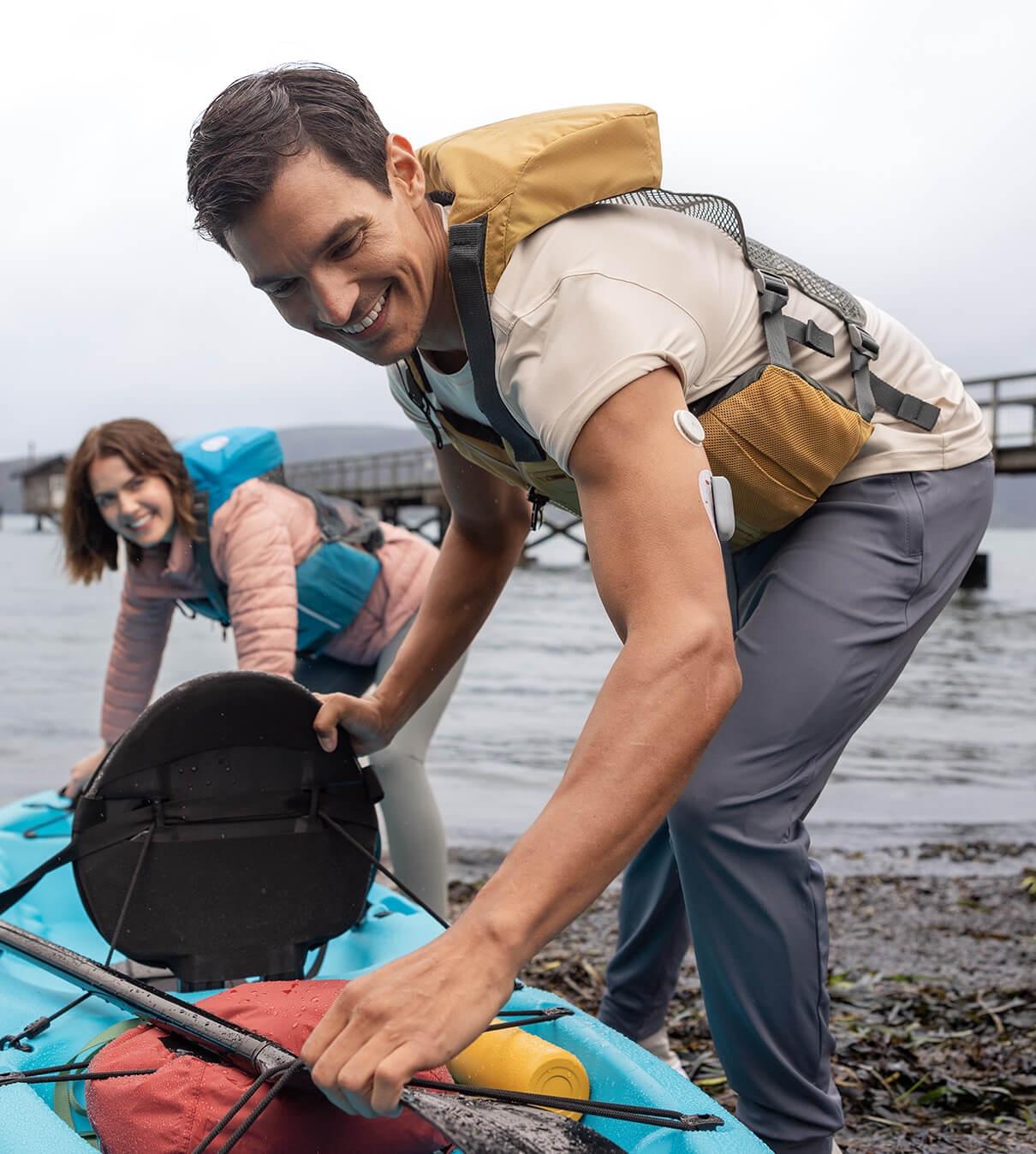 Man wearing a FreeStyle Libre 2 Plus sensor and Omnipod AID System pushing a kayak into the water with a woman behind him helping  