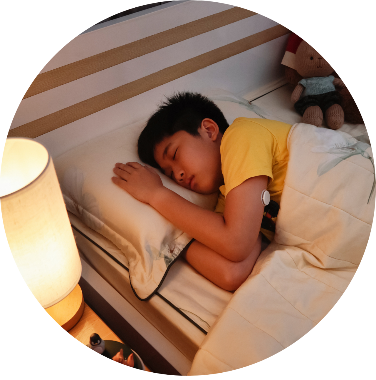 A boy sleeping in his bed with her sensor visible on his arm.