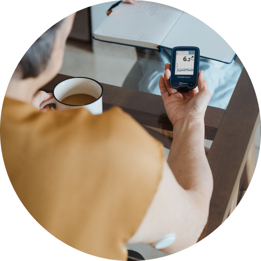 woman drinking coffee and looking at a glucose reader