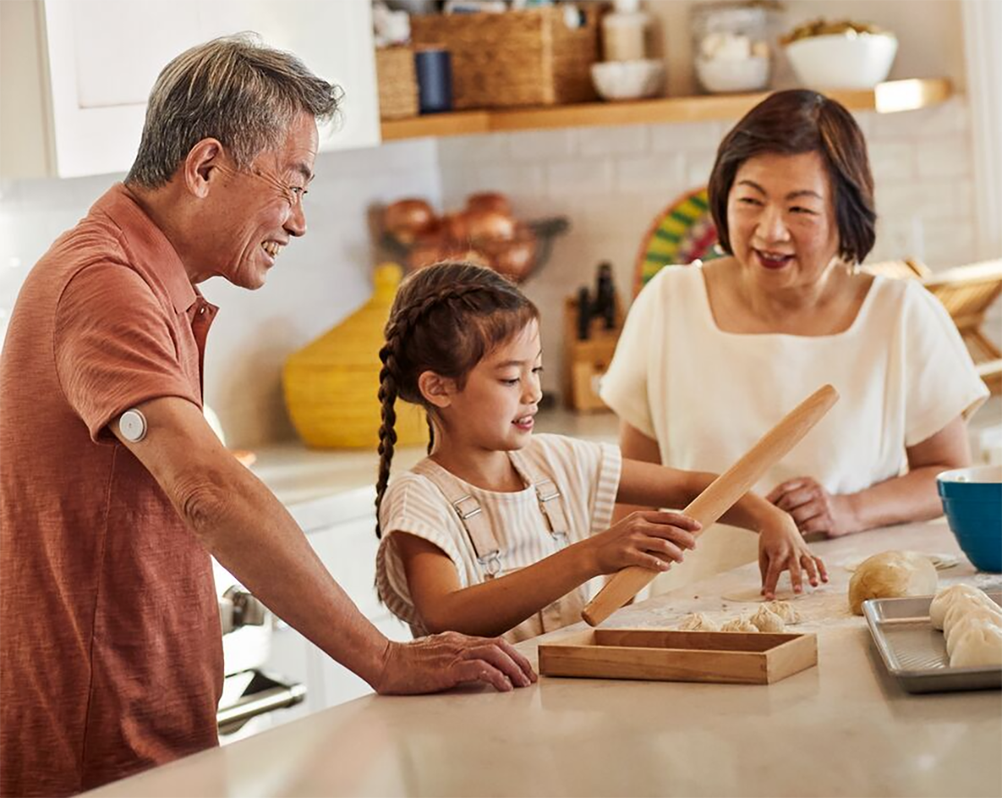 Oriental man wearing the Freestyle Libre while in the kitchen with his wife and child